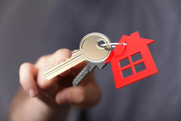 Person hand holding house key with red house keychain, conveying themes of home ownership, real estate, and mortgage. Perfect for housing, finan