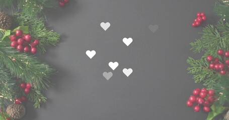 Framing six small white paper hearts on charcoal board with evergreen sprigs, red berries, lights