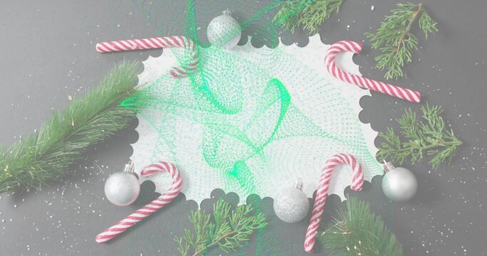 Showing white scalloped card with green mesh on gray table, candycanes, baubles, evergreen, snow - Powered by Adobe