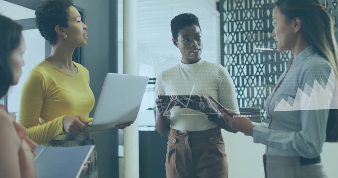 Discussing four women coworkers wearing yellow top, holding tablet, laptop in office, data overlays - Powered by Adobe