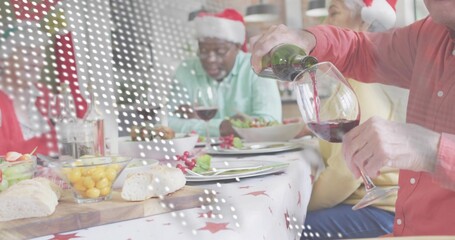 Pouring senior man red shirt Santa hat serving red wine at home dining table, copy space