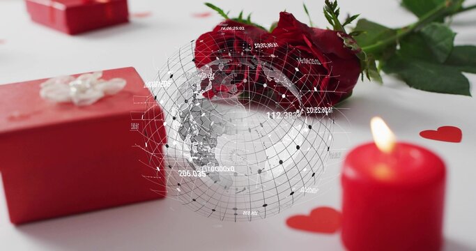 Fototapeta Displaying red rose lying on white tabletop, red gift box, lit candle, digital globe overlay