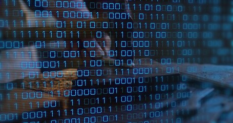 Leaning female analyst coding on laptop at dim desk, wearing dark top, glasses with binary code