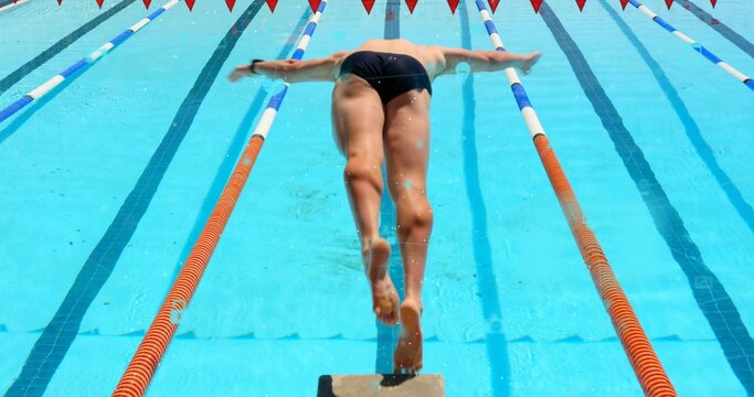 Diving male swimmer launching from block into outdoor pool, wearing dark briefs and lane ropes