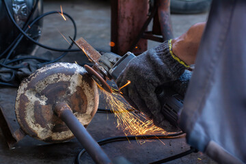 Close-up of industrial worker hands wearing gloves using an angle grinder to cut or polish rusty metal. Bright sparks flying in a workshop environment.