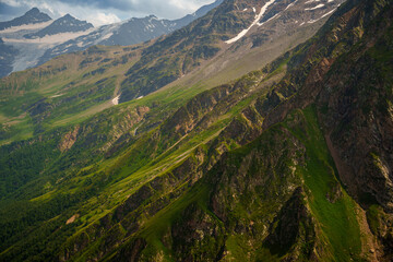 Green mountain slope with rocky cliffs and snowy peaks in the distance