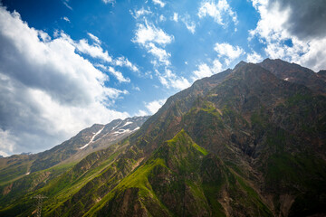 Naklejka premium Green mountain slope with rocky cliffs and snowy peaks in the distance