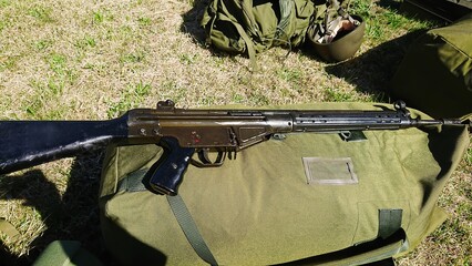 A vintage assault rifle rests on an olive drab duffel bag, with military gear in the background. This image conveys themes of combat, history, and tactical readiness.