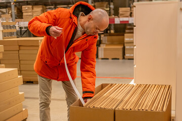 Fototapeta premium male customer measuring large flat cardboard boxes paper tape, self service furniture store warehouse aisle, home renovation interior, checking dimensions logistics planning, consumer shopping task