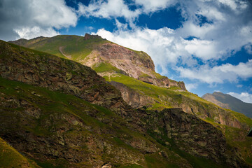 Obraz premium Green mountain slope with rocky cliffs and snowy peaks in the distance