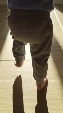 Barefoot infant learning toddler walking without any help first steps on a wooden floor, balance during walking Closeup back view