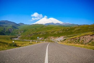 Road leading to Mount Elbrus with snow-covered peak and blue sky