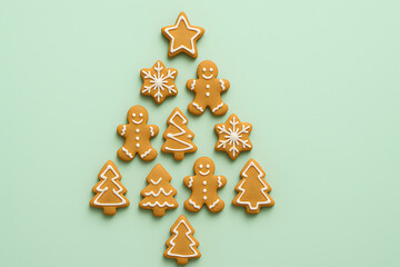 A collection of freshly baked gingerbread cookies, shaped like stars, snowflakes, Christmas trees, and gingerbread men, carefully arranged on a light mint green surface to form the outline of a Christ