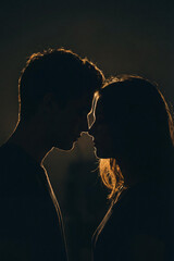 Silhouetted couple man and woman stands close in dramatic backlight, foreheads nearly touching. A moody, intimate moment of love, connection, and emotion captured in soft shadow and glow.