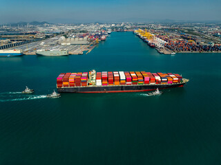 Aerial side view of large cargo ship sailing past busy industrial port terminal