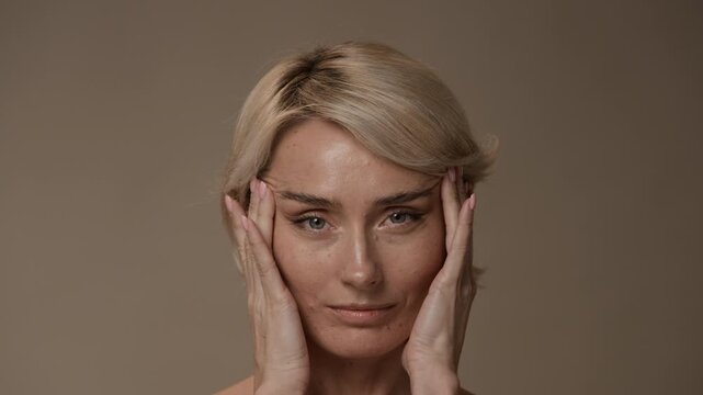 Close up of blonde woman looking at herself, squinting while massaging face slowly