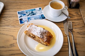 Savor a delicious slice of traditional apple strudel, dusted with powdered sugar, served with vanilla sauce in the beautiful Austria Alps, Kaprun. Perfect treat with coffee.