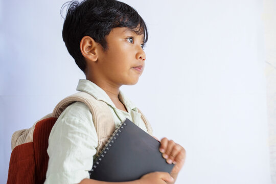 Side view portrait of an Asian preschool child wearing a backpack and holding a book, showing confident serious expression, isolated on white background. Back to school concept - Powered by Adobe