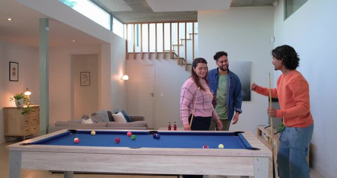 Three friends bantering and lining up shots around blue-felt pool table in living area for fun