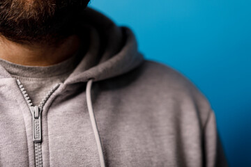 Close-up of a man wearing a grey Lacoste hoodie with a zipper against a blue background, perfect for fashion a © vegefox.com