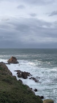 1080p footage of small ocean waves breaking and creating white foam on a rocky coastline in La Coru&ntilde;a, Spain. Cloudy afternoon with windy conditions.
