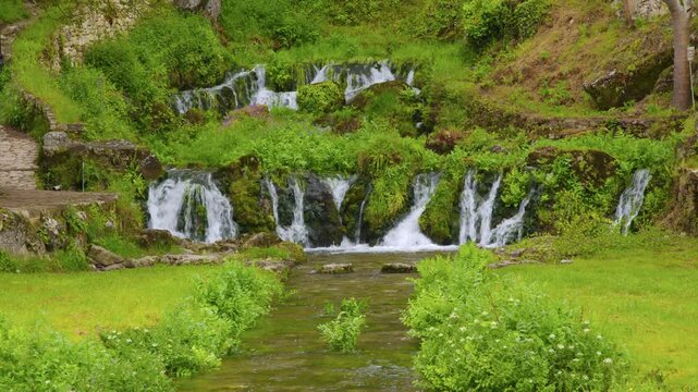 Peque&ntilde;as cascadas que descienden entre rocas y vegetaci&oacute;n en un paisaje natural luminoso y sereno.