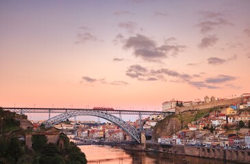 A magnificent view showcasing the Dom Luis I Bridge spanning a river in Porto, Portugal, bathed in the soft, pastel hues of a breathtaking sunset