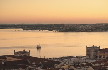 The sun paints the sky with gentle hues. A sailboat sails on the shimmering waters of the Tagus...
