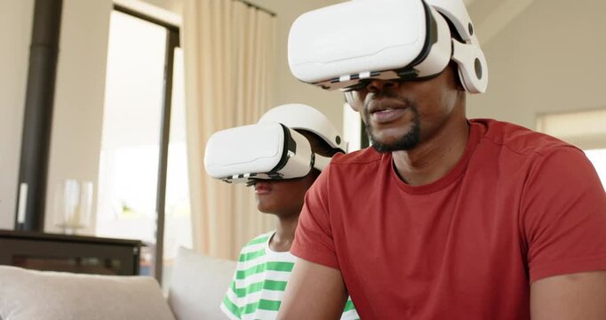 African American father and son putting VR headsets gripping controllers reacting to game at home