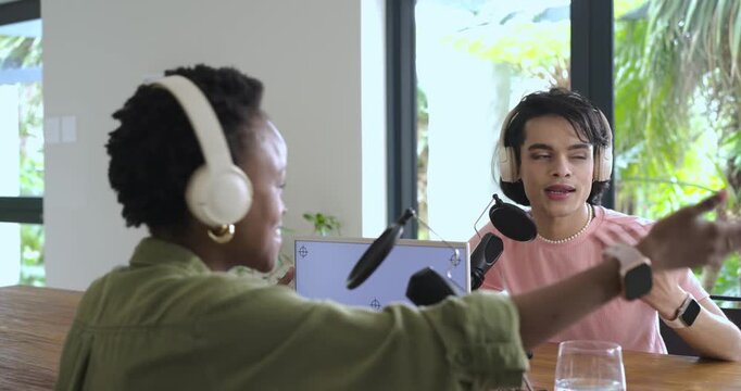 Diverse coworkers recording podcast in studio with man gesturing into mic then woman interjecting