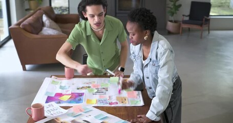 Diverse coworkers kicking off brainstorming by arranging sticky notes on paper at studio table