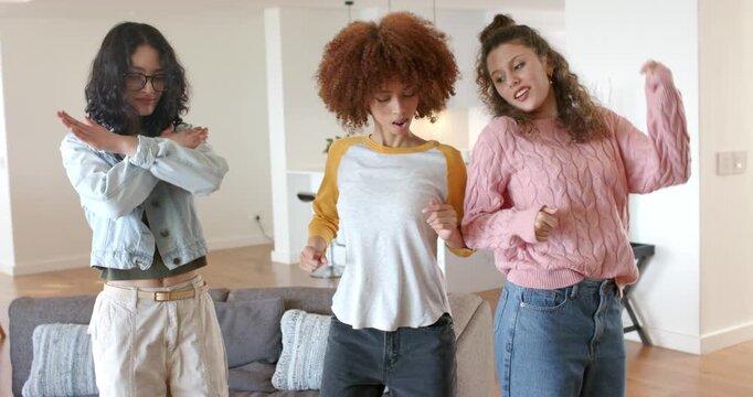 In living room, diverse female friends tracing arms, squatting and ending synchronized pose by sofa