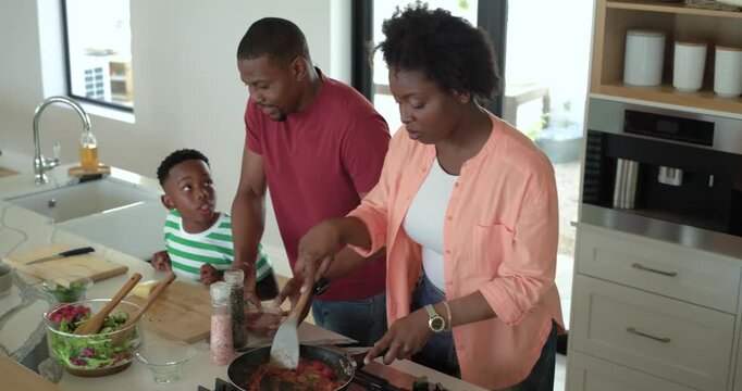 African American family at counter with father bringing sauce and mother stirring it for tasting