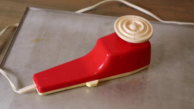 Vintage red and cream handheld electric massager on a metal tray, featuring a circular head and visible power cord.