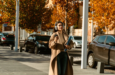 Naklejka premium Woman Walking with Headphones and Coffee in Autumn City
