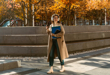 Naklejka premium Woman Walking with Headphones and Coffee in Autumn City