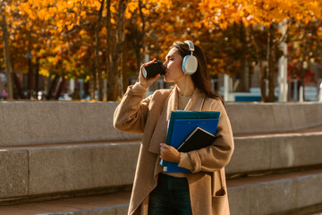 Naklejka premium Woman Walking with Headphones and Coffee in Autumn City