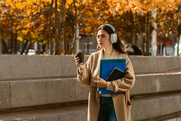 Naklejka premium Woman Walking with Headphones and Coffee in Autumn City