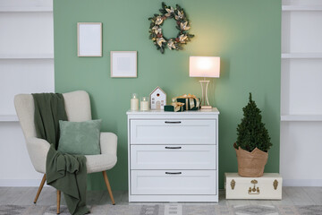 Christmas decor on white dresser and fir tree near green wall indoors. Interior design