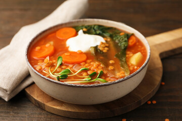 Tasty lentil soup with sour cream and vegetables in bowl on wooden table, closeup