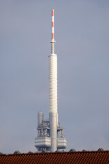 Tall telecommunications tower with antennas rising above rooftops against a clear sky. Broadcasting infrastructure, signal transmission technology, vertical structure, and urban communication network.