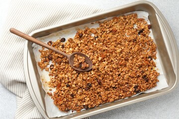 Tasty granola with dried fruits and spoon in tray on light grey table, top view