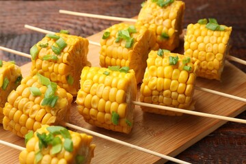 Skewers with pieces of boiled corncobs and green onion on wooden table, closeup