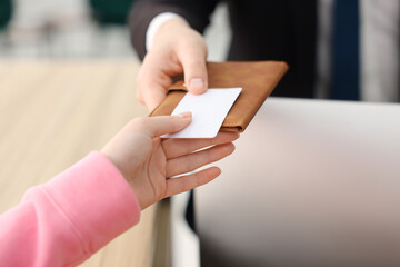 Receptionist giving passport and hotel key card to guest at reception desk indoors, closeup