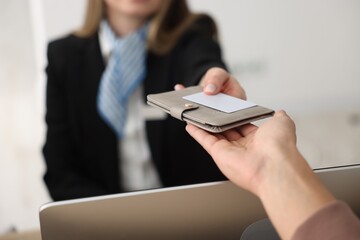 Receptionist giving passport and hotel key card to guest at reception desk indoors, closeup