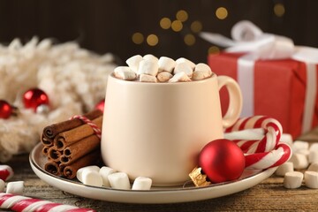 Tasty cocoa with marshmallows, candy canes, cinnamon and Christmas decor on wooden table, closeup