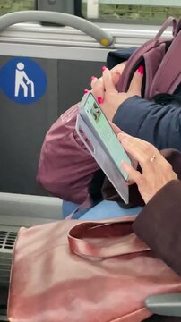 woman reading ereader on train seat with pink nails and leather bag near priority sign, closeup of hands tapping tablet, quiet