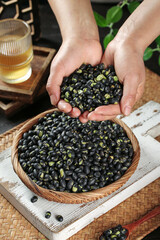Fresh Black Beans in Hands from Wicker Basket on Rustic Wood Table