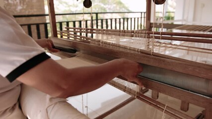 Close-up of woman weaving silk fabric on a traditional handloom using ancient weaving techniques, surrounded by nature, Cambodia, Siem Reap.