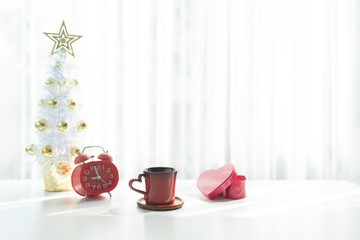 Red coffee cup and red gift box and Christmas tree decor arranged on white table